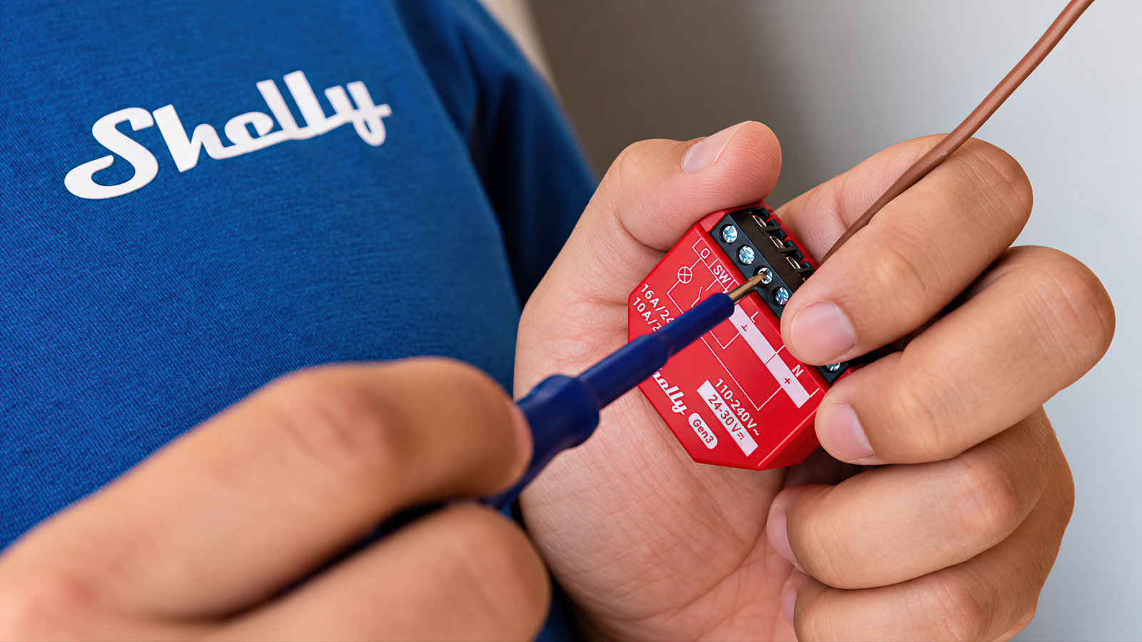 Hands fitting a wire into a Shelly Gen3 relay in front of a Shelly T-shirt