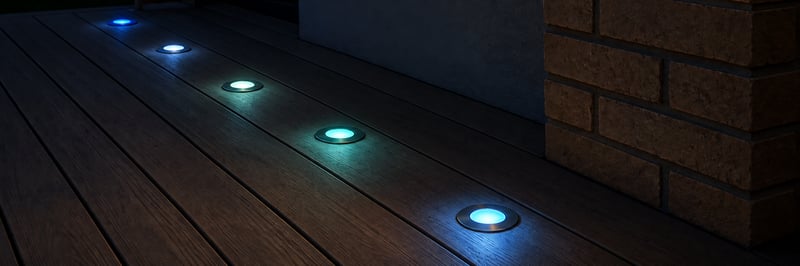 A timber deck at night with a row of recessed deck lights glowing blue and white along the boards.
