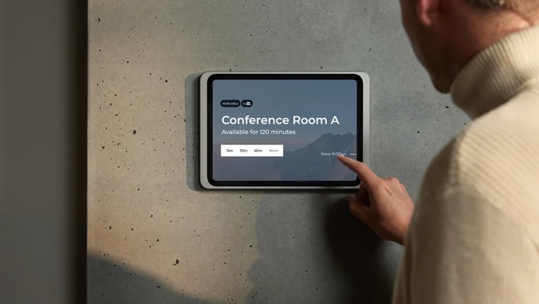 Displine Dame Wall 2.0 in silver holding an iPad on a concrete wall, with a person tapping a meeting room booking screen
