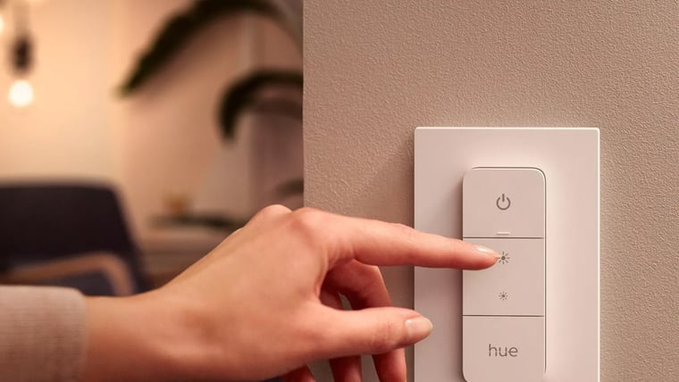 A hand pressing a Hue dimmer switch on a wall