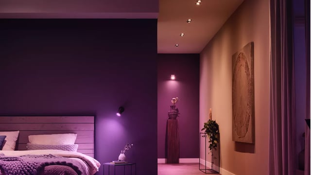 A hallway with downlights leading into a bedroom, lit low in purple and pink